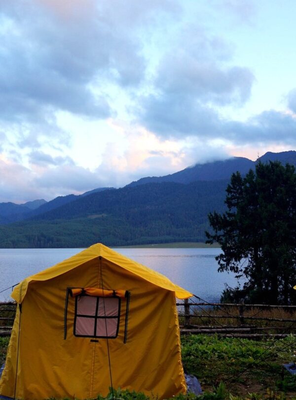 Camping tent set up near the tranquil shores of Rara Lake surrounded by forested hills in Nepal