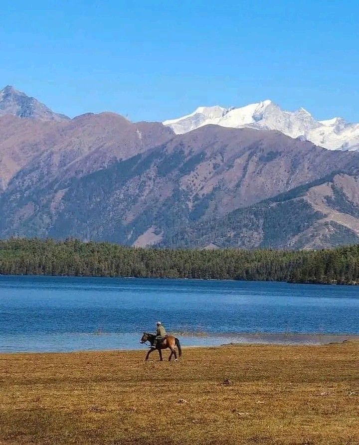 Tourist riding a horse along the shore of Rara Lake with mountains in the background