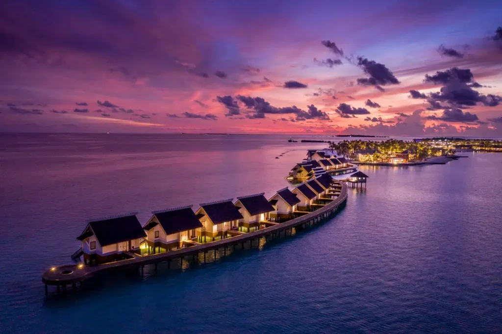 Romantic night view of overwater villas at SAii Lagoon Maldives with pink sky reflecting on the ocean