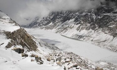 Frozen surface of Tsho Rolpa Glacial Lake surrounded by snow-covered Himalayan peaks