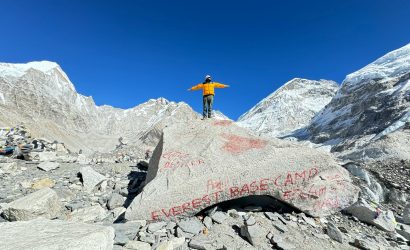 Tourist posing at Everest Base Camp surrounded by Himalayan peaks.