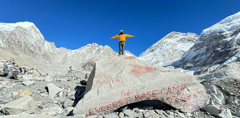 Tourist posing at Everest Base Camp surrounded by Himalayan peaks.